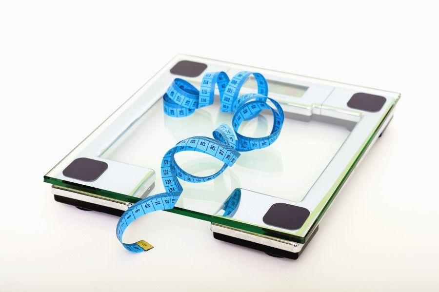 Soft measuring tape on top of clear glass digital bathroom scale